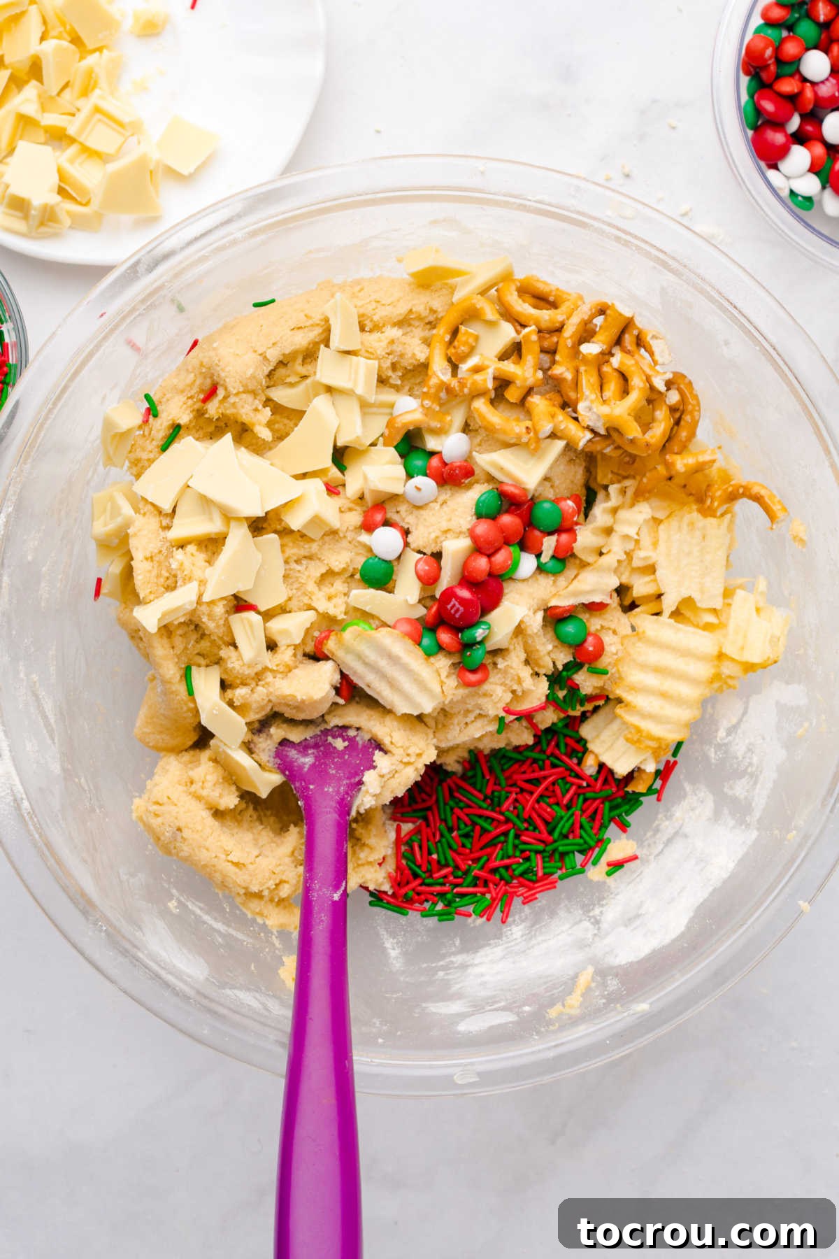 Stirring pretzels, potato chips, and candies into cookie dough in mixing bowl. 