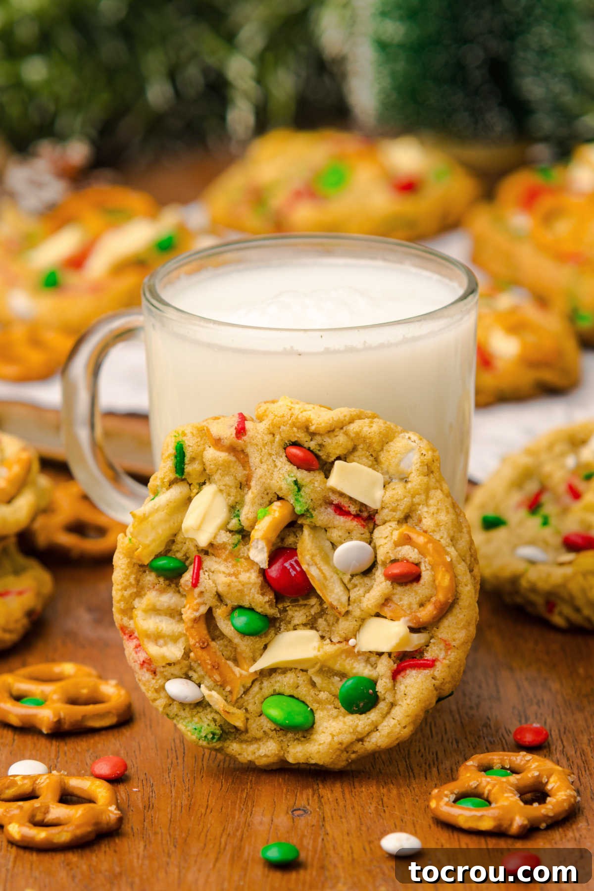 Christmas kitchen sink cookie leaned up against a mug of white hot chocolate, ready to enjoy. 