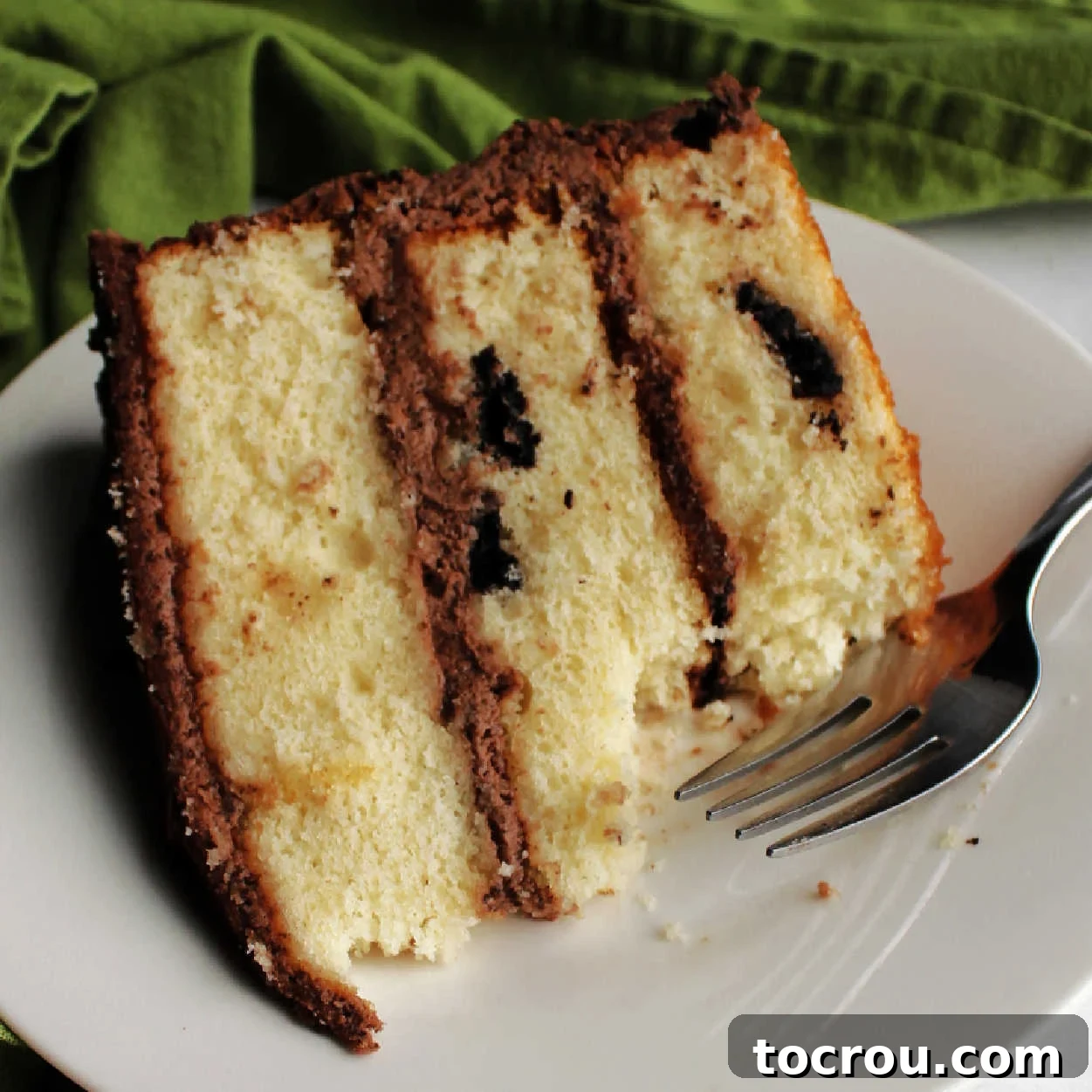 This cake boasts three deliciously easy layers, generously dotted with your favorite chocolate sandwich cookies for the perfect cookies and cream cake experience. Close-up shot of a magnificent slice of cookies and cream cake, revealing its moist white cake layers infused with crushed Oreos, all beautifully coated in a rich chocolate frosting.