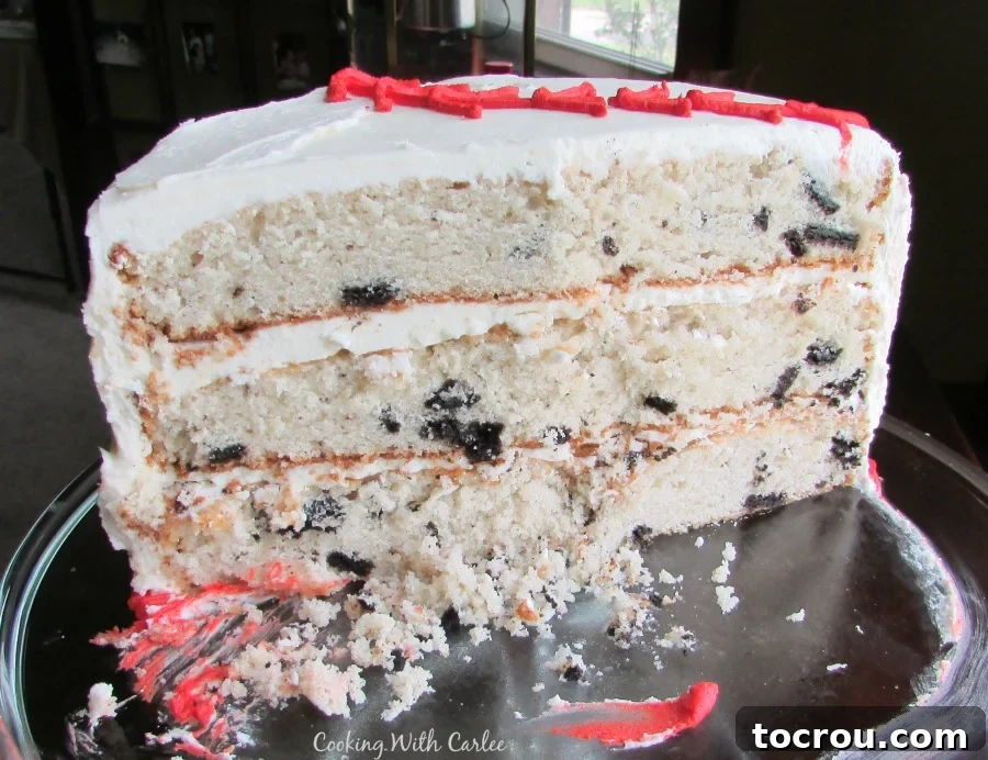 Every mouth-watering slice reveals the delightful combination of tender cake and crunchy crushed cookies. An inviting inside view of a three-layer cookies and cream cake, clearly showcasing the speckled white cake and distinct frosting layers.