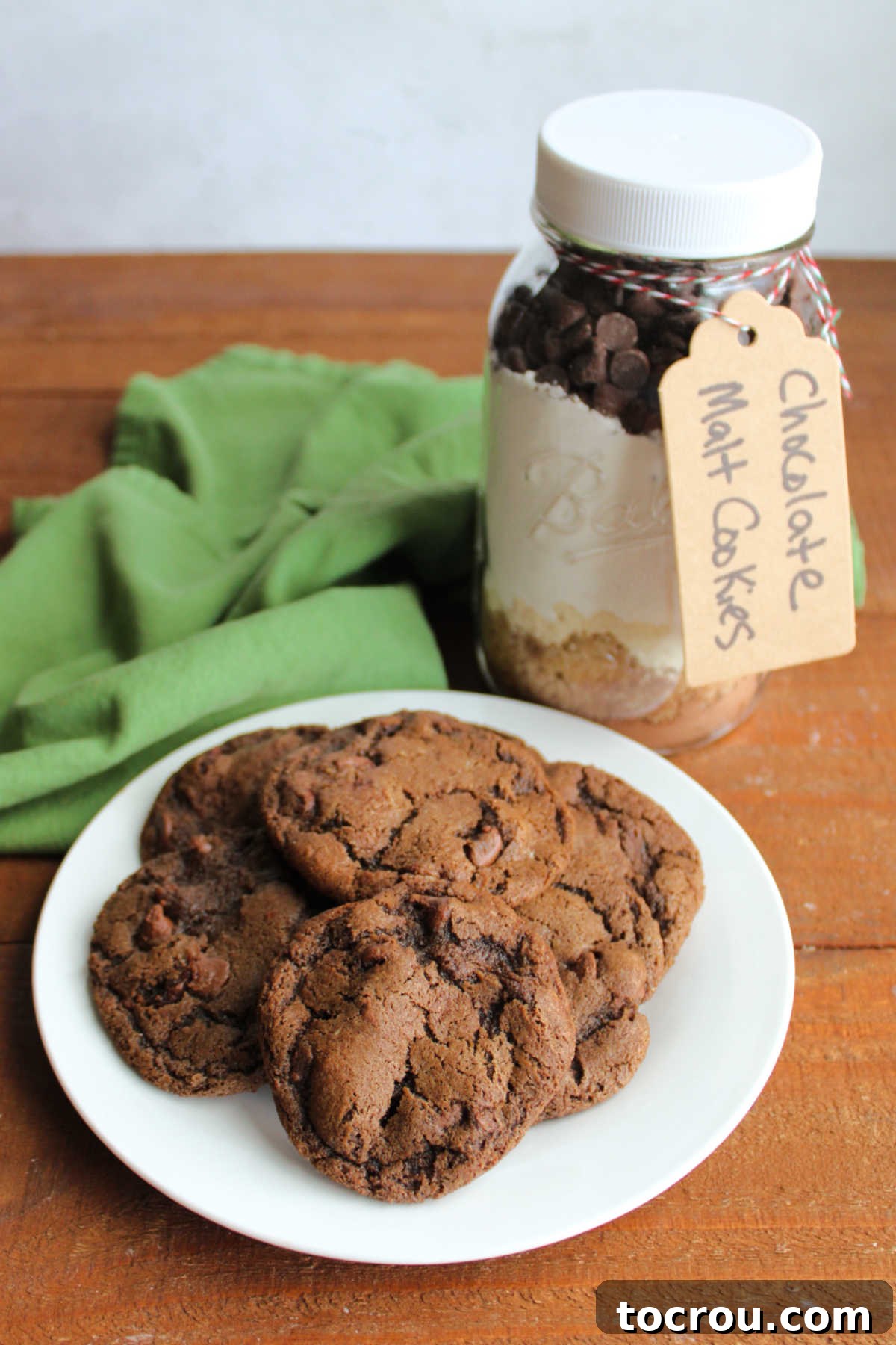 A charming jar of chocolate malt cookie mix is displayed alongside a plate of freshly baked chocolate malt cookies, ready to be enjoyed.