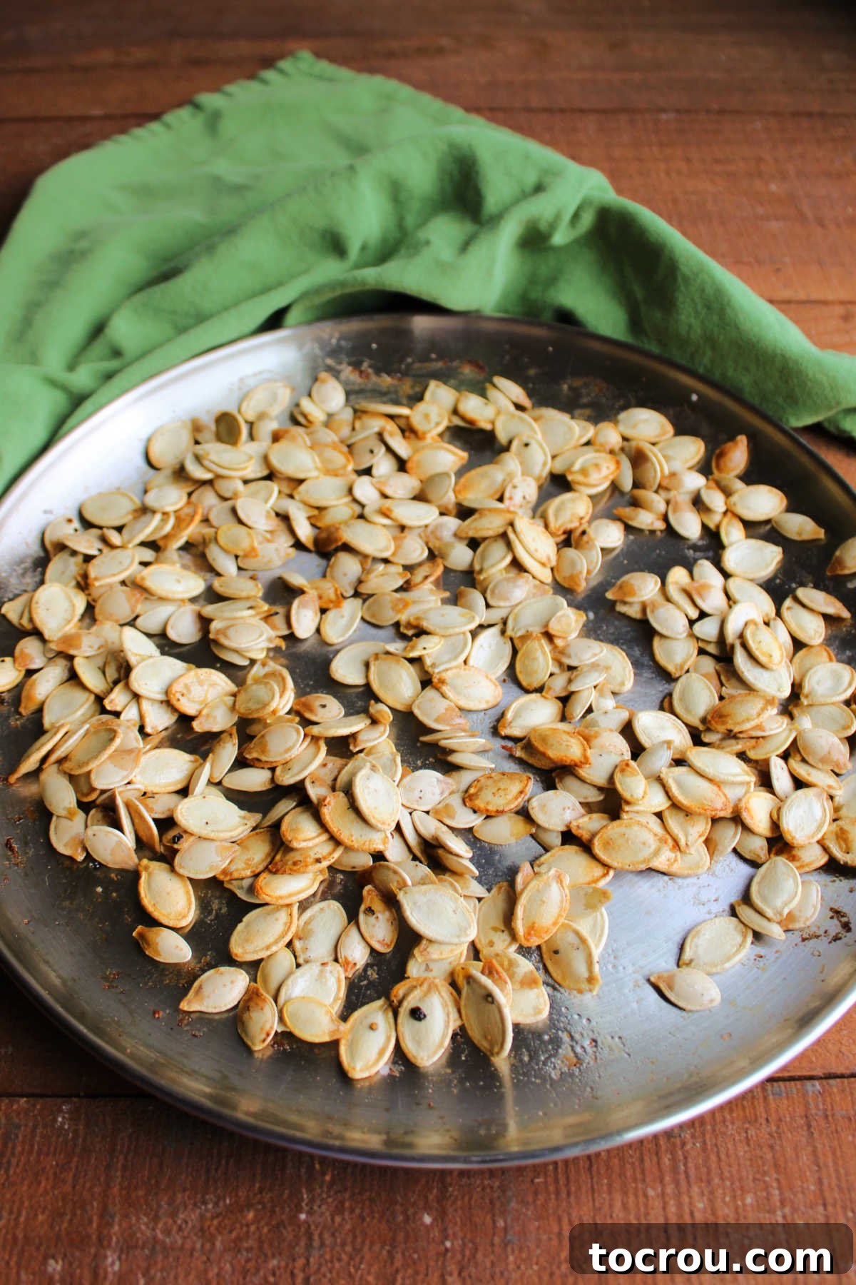 Crunchy Pumpkin Perfection 3 Stainless steel pizza pan covered in roasted pumpkin seeds showing a light golden color and roasted appearance.
