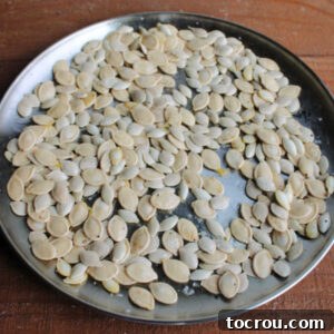 Pumpkin seeds coated in oil, salt, garlic powder, and pepper on a pan, ready to roast.