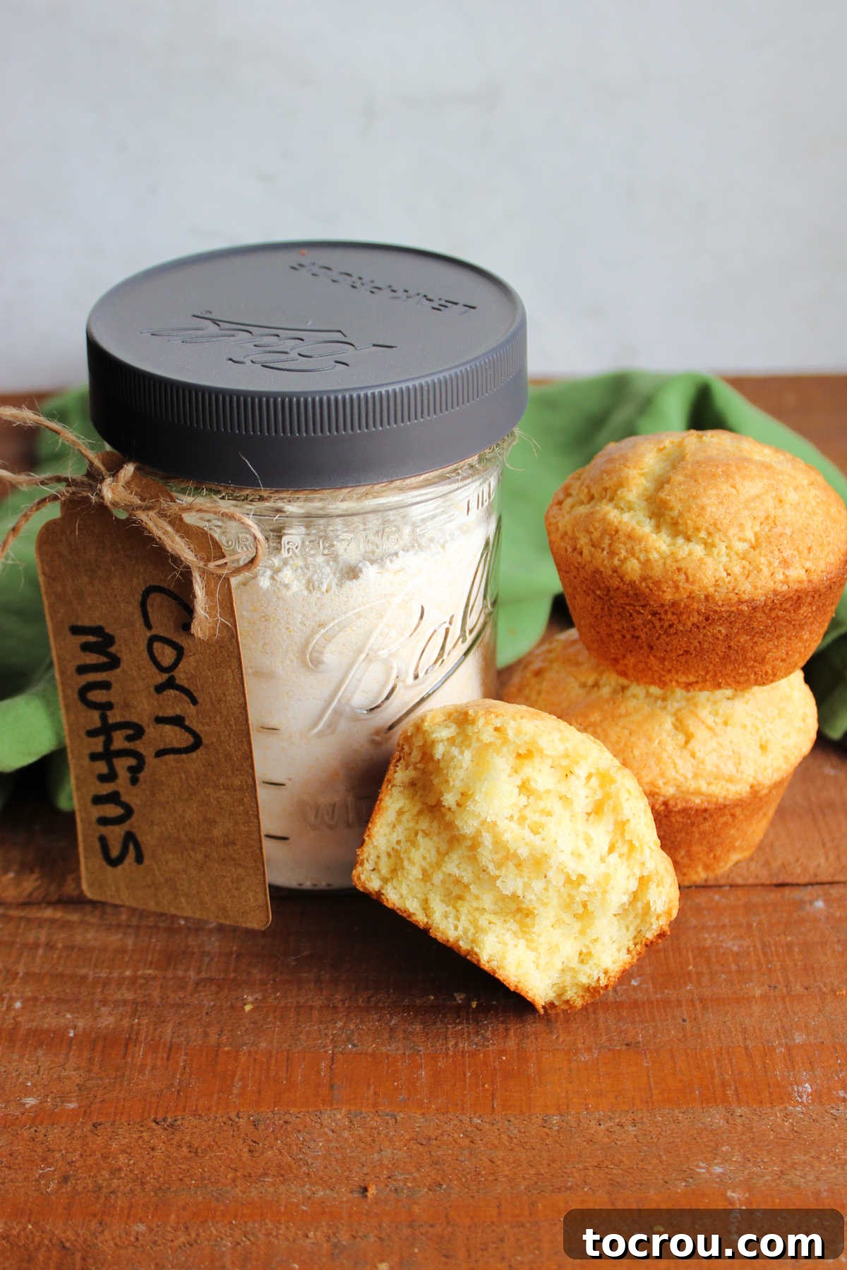 Corn Muffin Mix Jar and Fresh Muffins Wide mouth pint jar with corn muffin mix inside next to a half of a corn muffin showing airy interior and a couple of more freshly baked corn muffins.