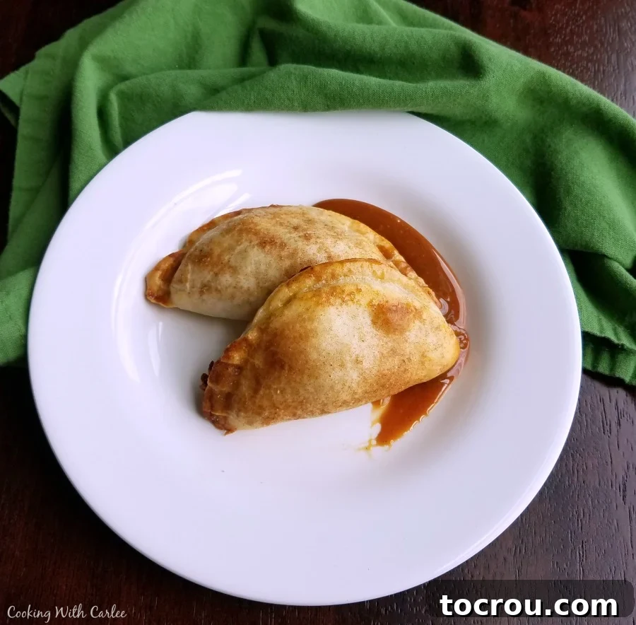 Smear of caramel on plate topped with two golden brown empanadas filled with caramel apple filling.