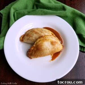 Smear of caramel on plate topped with two golden brown empanadas filled with caramel apple filling.