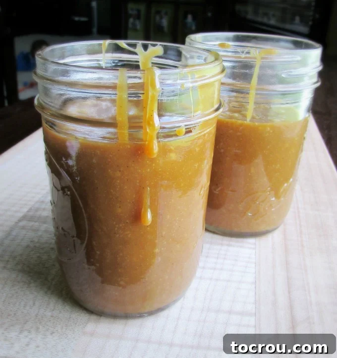 Homemade Cajeta: Liquid Gold Caramel Sauce Two jars of golden goat's milk cajeta, with a luscious drip running down the side of the front jar, hinting at its rich texture and irresistible sweetness.