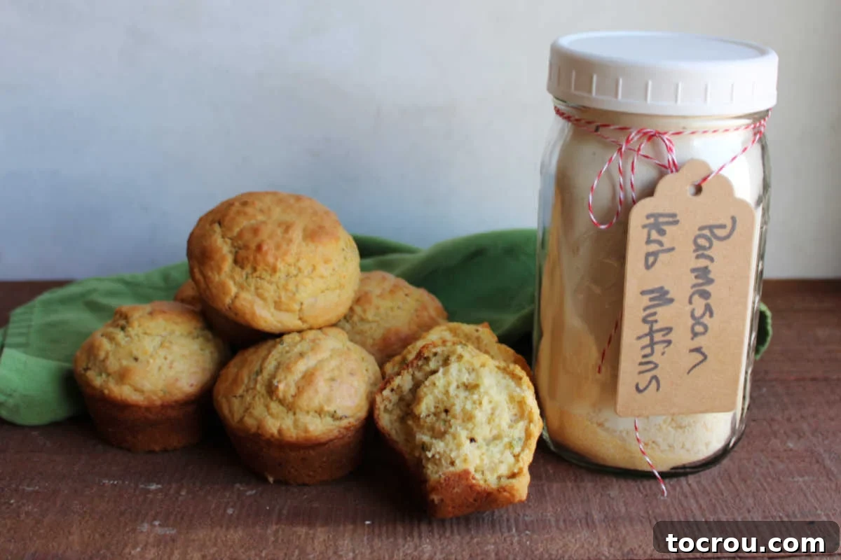 Quart jar filled with dry ingredients to make savory muffins with a gift tag that says parmesan herb muffins next to a pile of muffins, one ripped in half showing the fluffy interior.