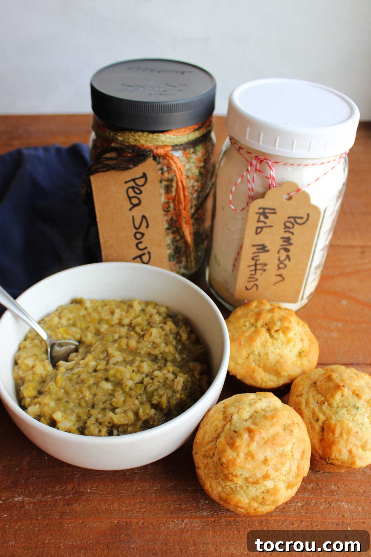 Jar of parmesan herb muffin mix next to a jar of pea soup mix with a bowl of soup and freshly baked muffins nearby.