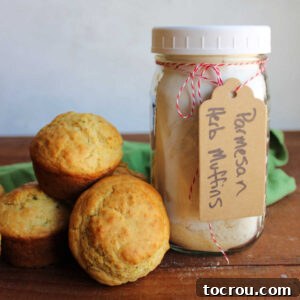 Jar of homemade parmesan herb muffin mix next to a small pile of freshly baked savory muffins.