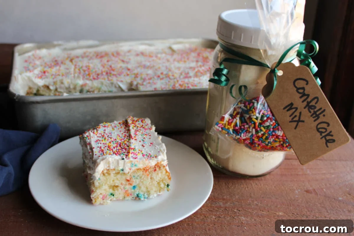 Homemade Confetti Cake Mix in a Jar Slice of homemade confetti cake with whipped frosting and colorful sprinkles, placed next to a decorative jar filled with homemade cake mix, adorned with a tag and a small bag of sprinkles.