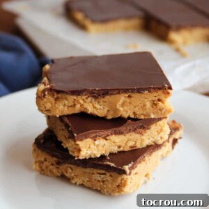 Stack of three buckeye bars with crunchy rice krispie and peanut butter layer on the bottom and a chocolate shell on top.