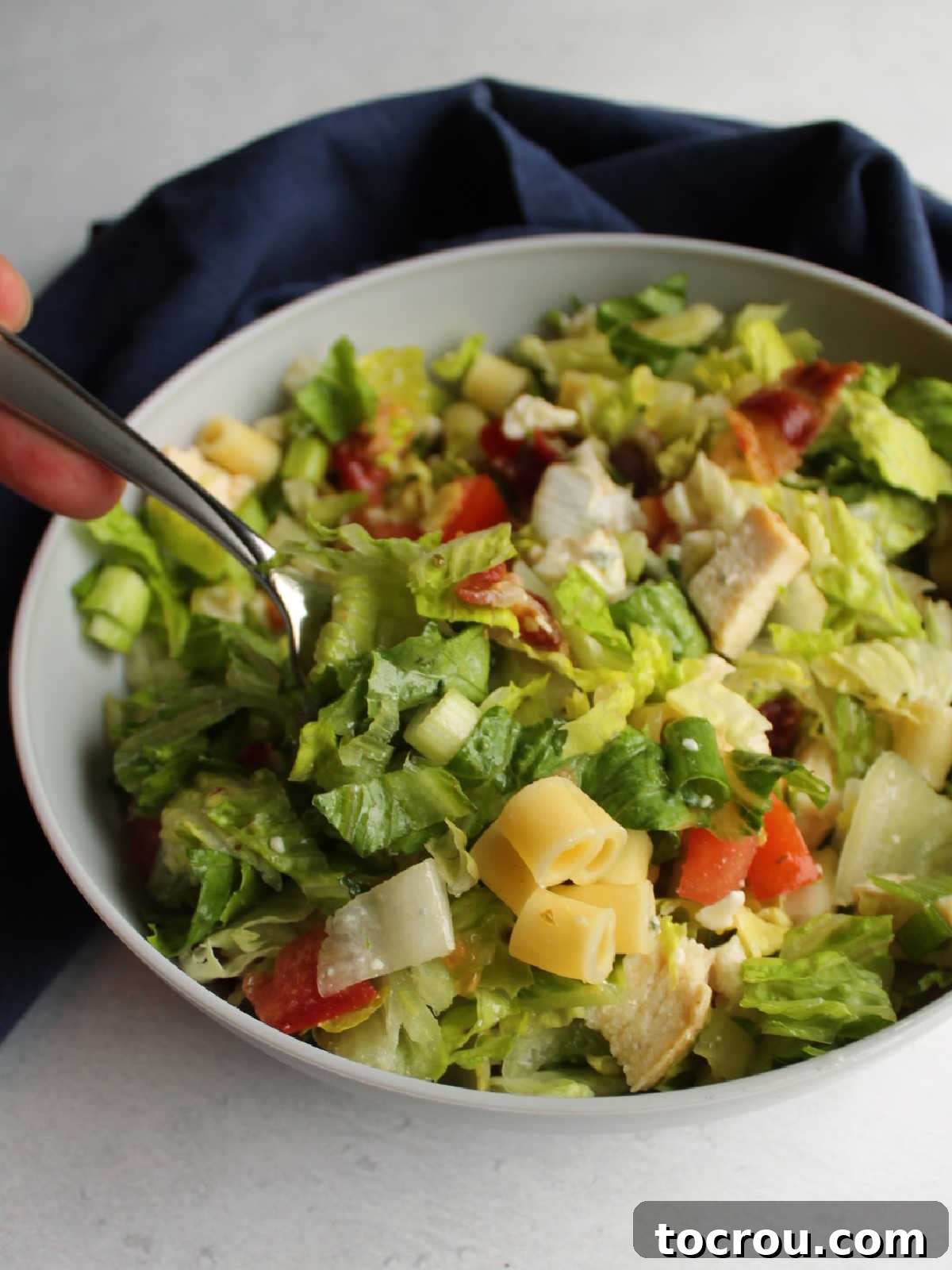 Chicago Chopped Salad Classic 3 Fork getting a bite of chopped salad out of a bowl showing greens, pasta, chicken, cheese, tomatoes and more.