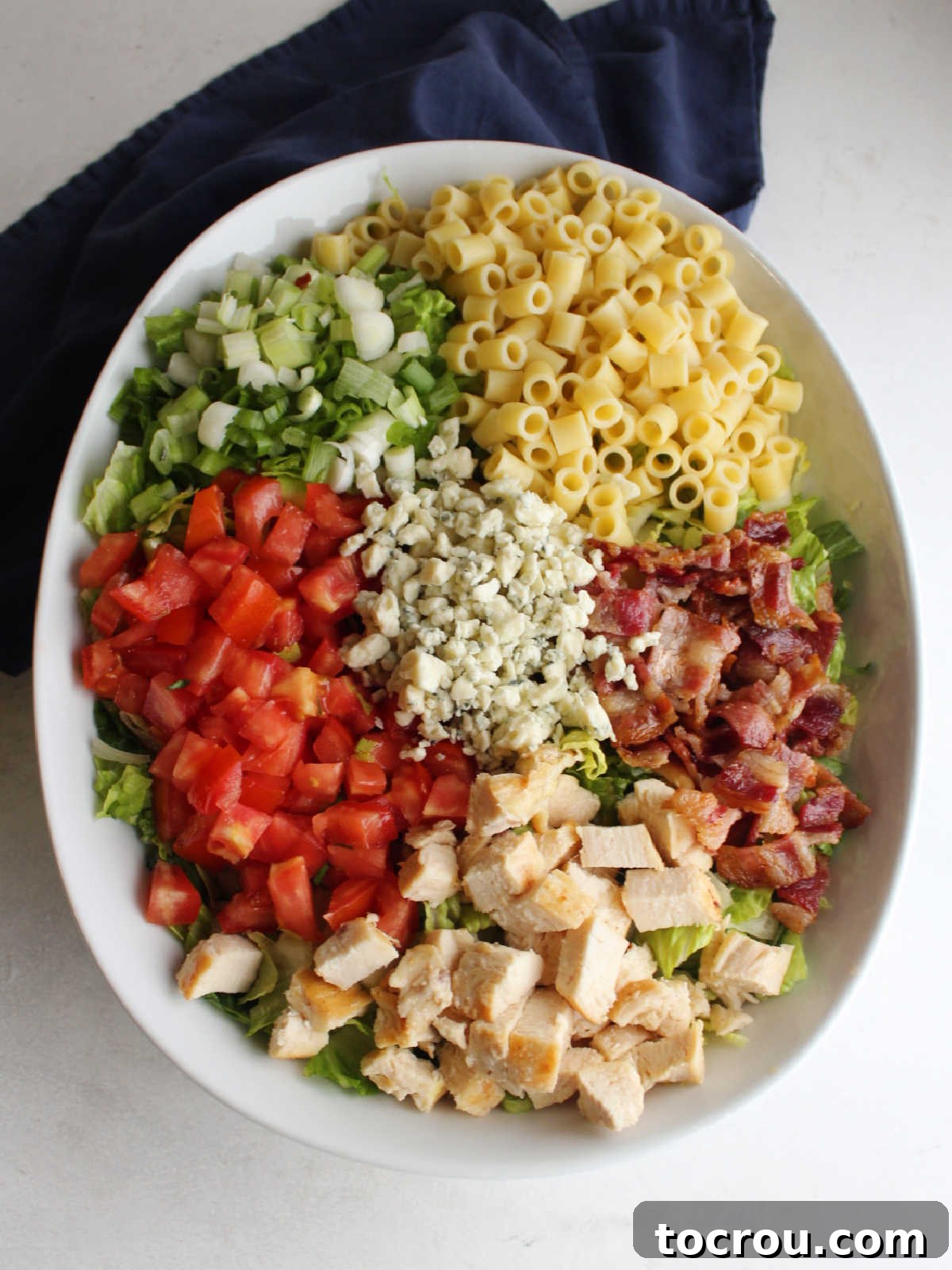Chicago Chopped Salad Classic 7 Large serving bowl filled with chopped lettuce topped with crumbled bacon, chopped chicken, diced tomatoes, sliced green onions, pasta, and gorgonzola.