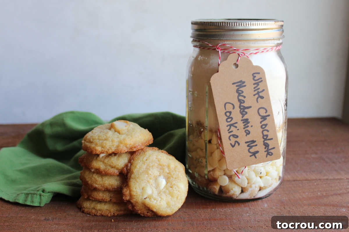 Stack of freshly baked white chocolate macadamia nut cookies next to a quart jar of cookie mix. 