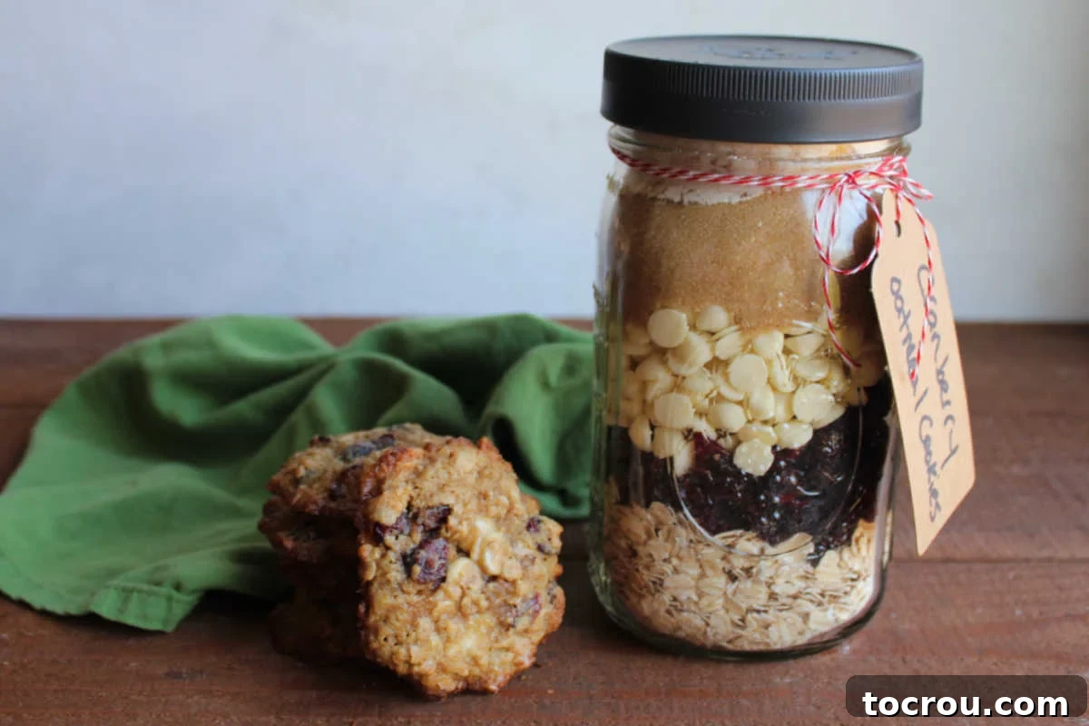 White Chocolate Cranberry Oatmeal Cookies In A Jar Mix White chocolate cranberry oatmeal cookies next to a jar of mix. A beautifully layered jar of dry cookie mix sits beside a plate of golden-brown cookies, showcasing the delightful outcome of this easy recipe.