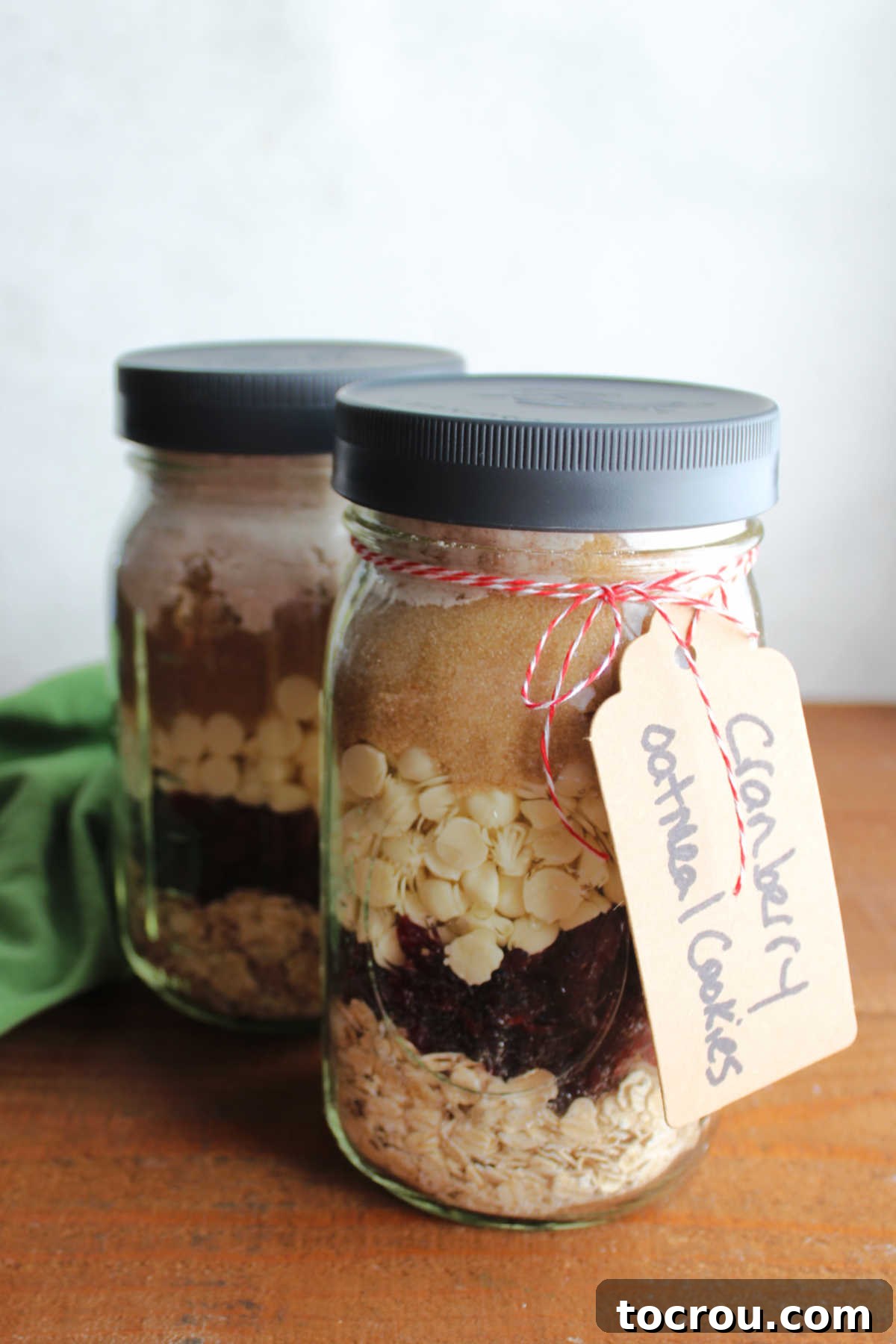Cranberry Oatmeal Cookie Mix Jars Glass quart jars filled with layers of oatmeal, craisins, white chocolate chips, brown sugar, sugar, and flour mixture with tag that says cranberry oatmeal cookies. These beautifully layered jars are ready to be stored or gifted, making preparation a breeze for homemade treats.