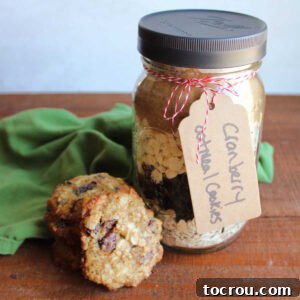 Cranberry Oatmeal Cookies In A Jar Jar of cranberry oatmeal cookie mix with white chocolate chips next to a stack of cookies baked from the mix.