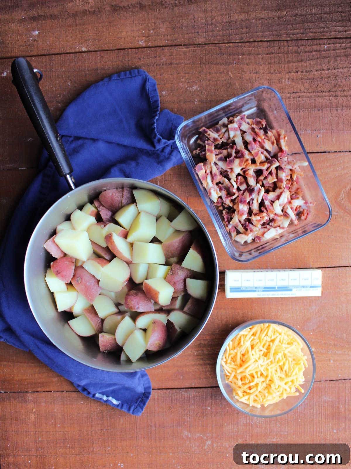 Ingredients including shredded cheddar, butter, chopped bacon and boiled chunks of potatoes.