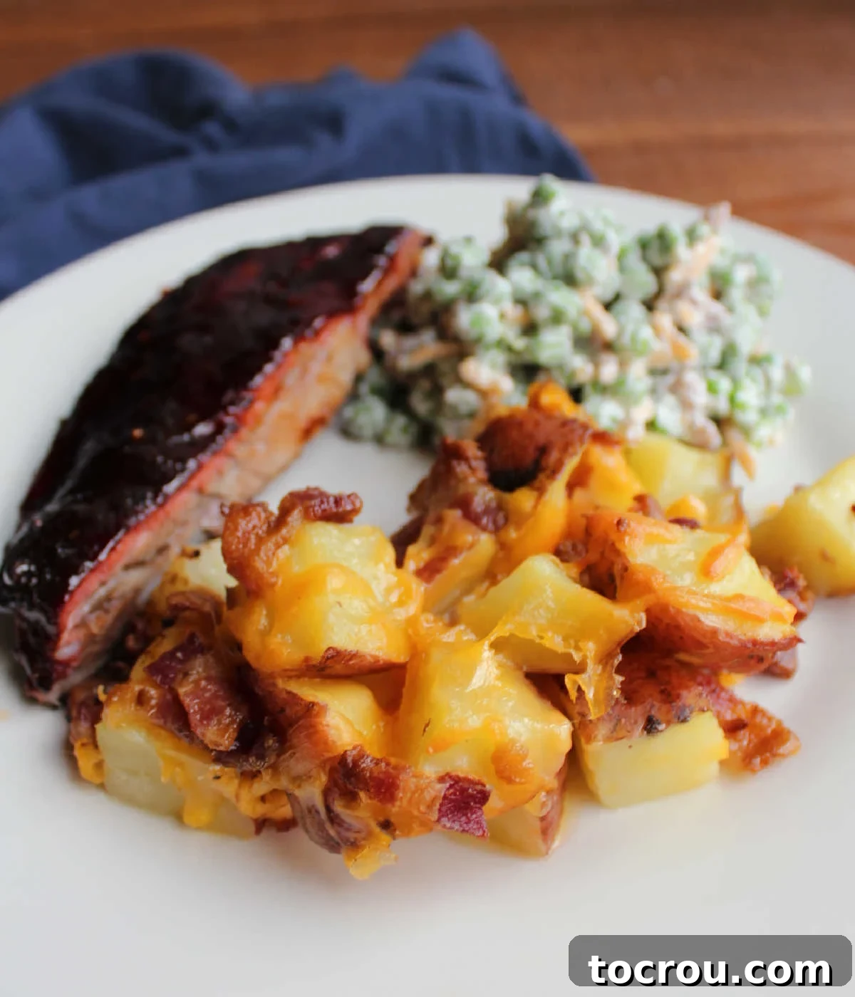 Serving of potato casserole with cheese and bacon on plate with bbq ribs and some pea salad.