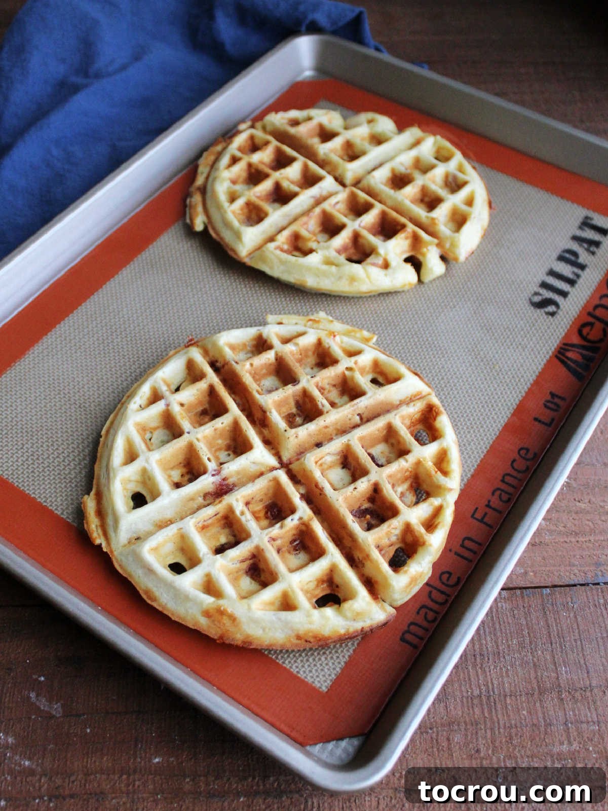 Waffled Croque Madame 6 Golden brown savory waffles with bits of ham and cheese inside on a silicone mat lined baking pan.