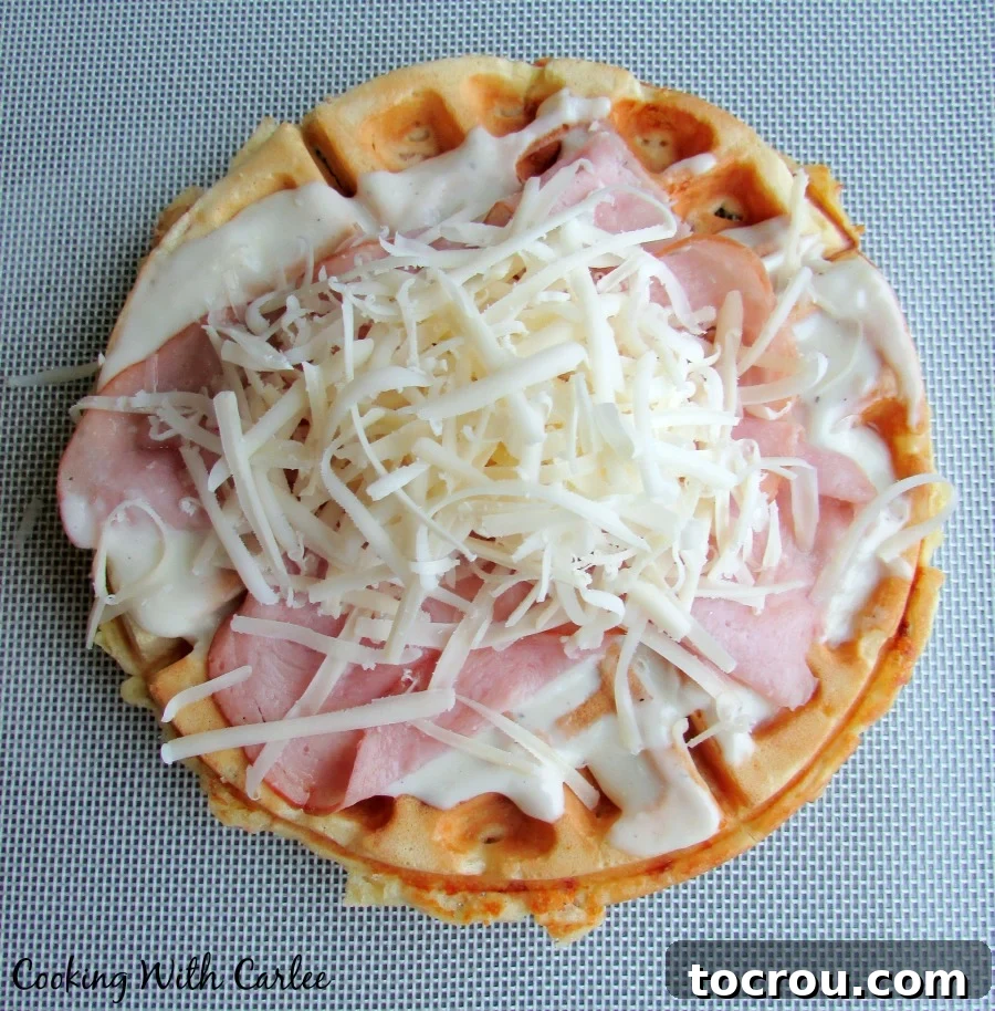 Waffled Croque Madame 8 Waffle topped with white sauce, ham and cheese ready to go into the oven for broiling.