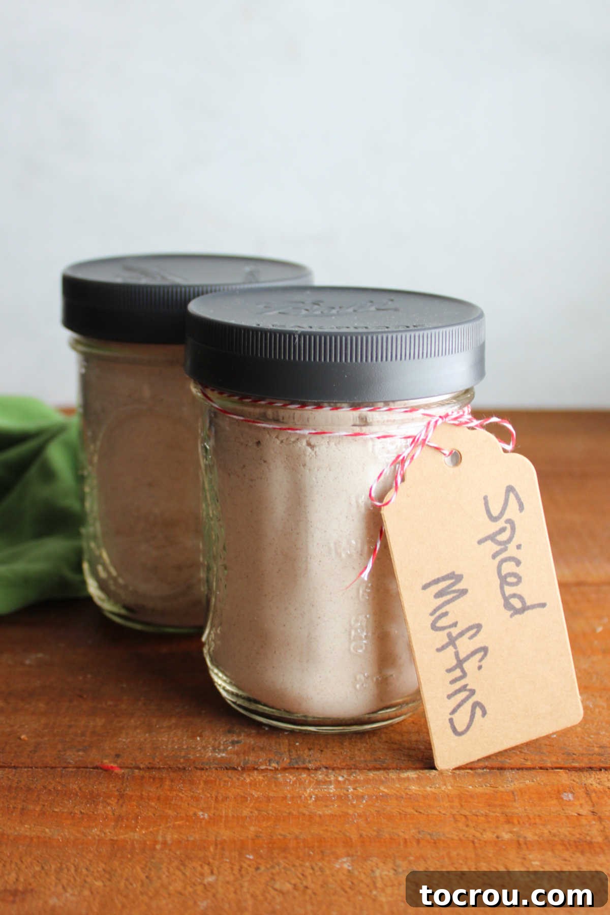 Two clear glass pint jars filled with layers of homemade spiced muffin mix, each with a charming tag indicating its contents, beautifully arranged as edible gifts.