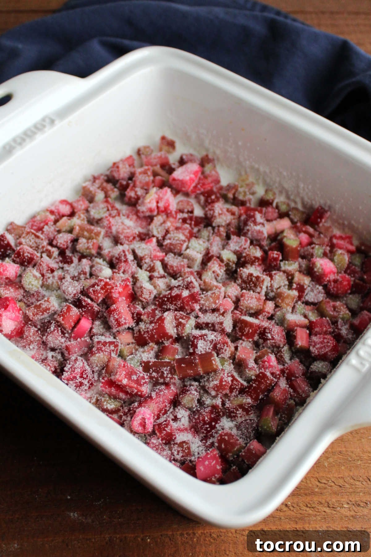 Chopped rhubarb in a square baking dish with sugar.