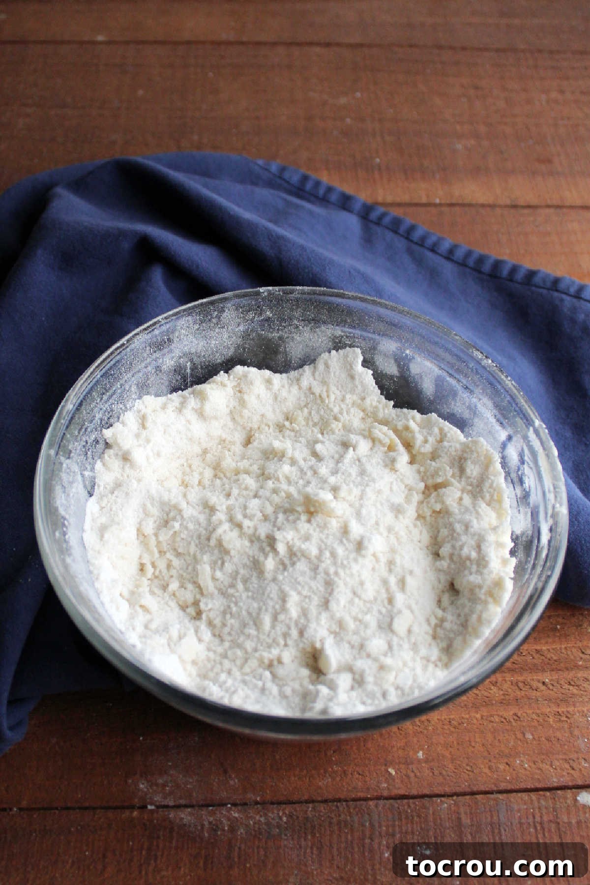 Butter cut into flour, sugar and baking powder mixture making coarse crumbs.