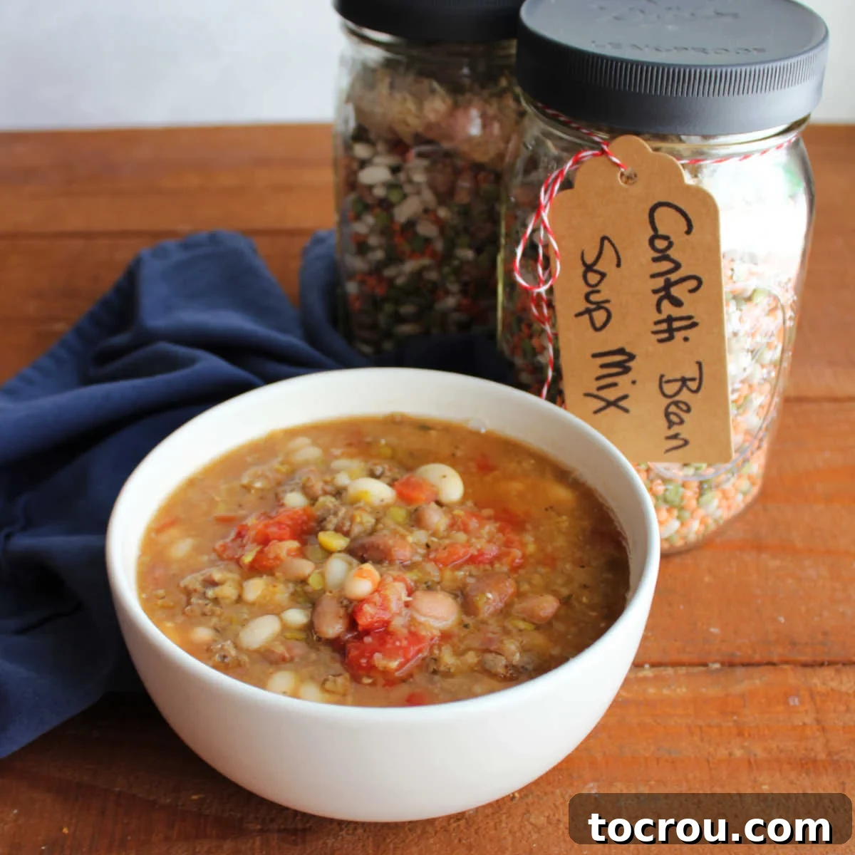 Bowl of confetti bean soup next to a couple of jars of homemade bean soup mix.
