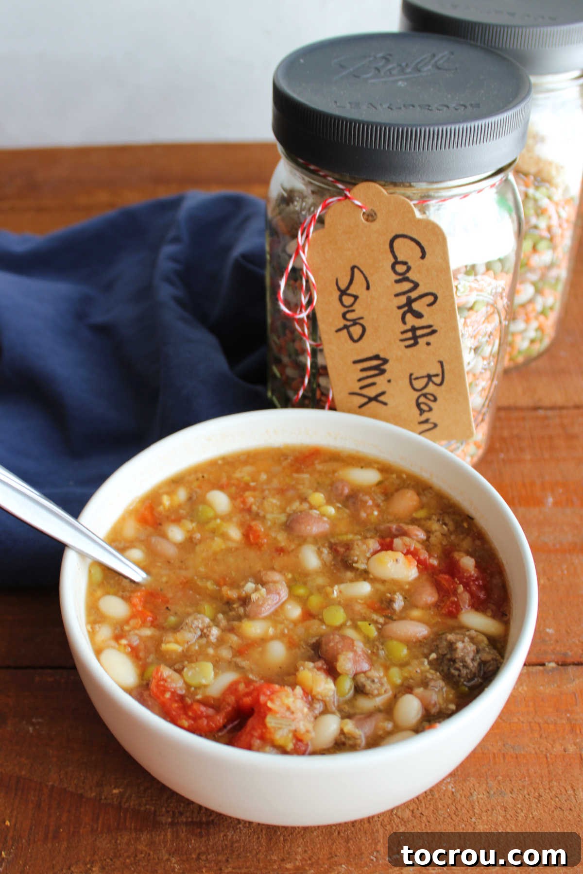 Bowl of confetti bean soup next to a couple of quart jars with homemade bean soup mix inside.