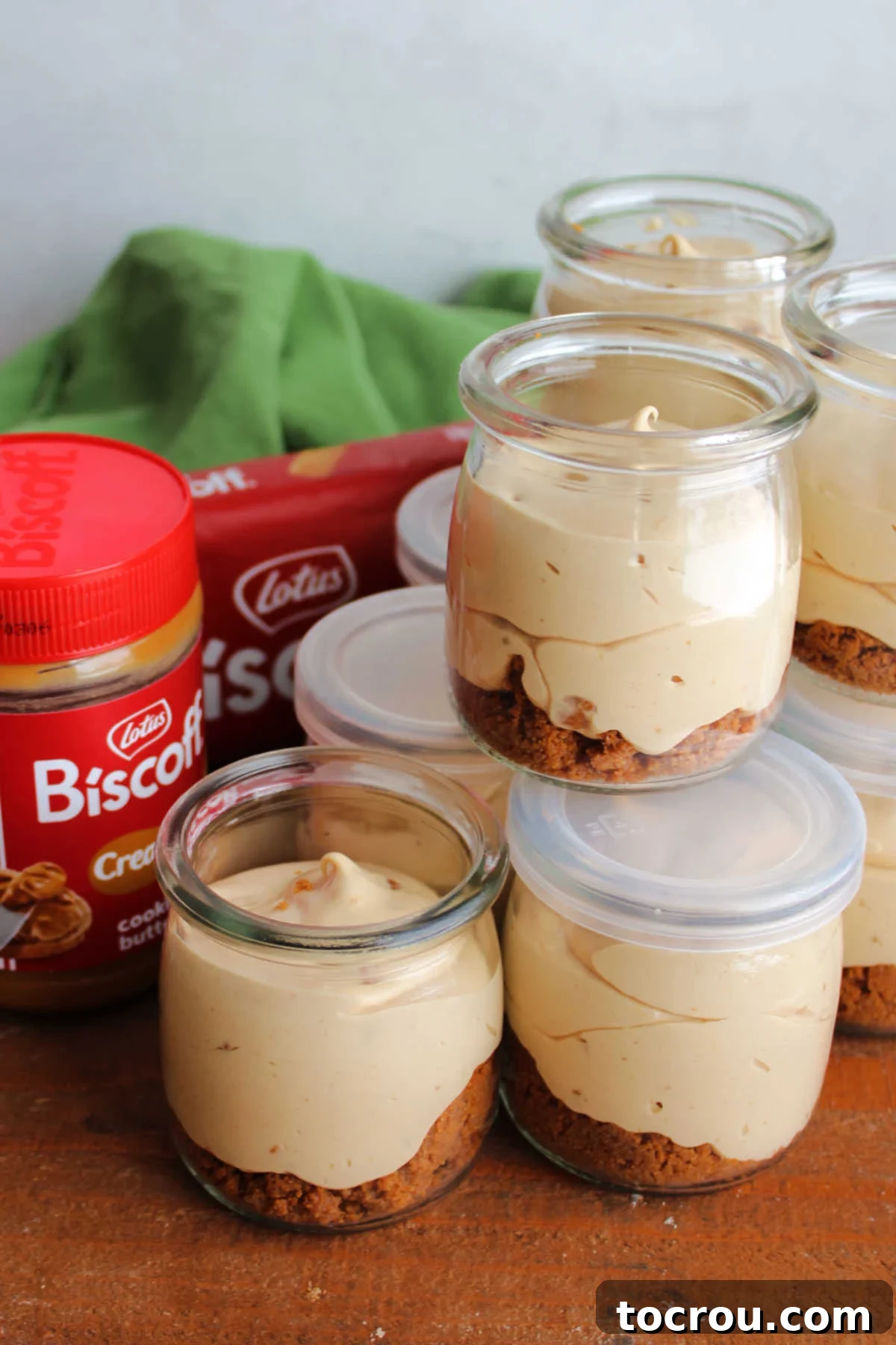 Jars of no bake Biscoff cheesecake with a jar of cookie butter and some Biscoff cookies in the background.