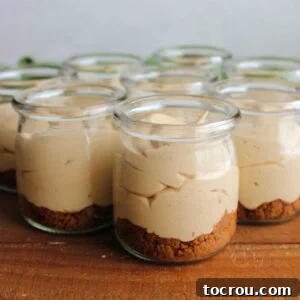 Small glass jars filled with no bake cookie butter cheesecake mixture and a Biscoff cookie crust.