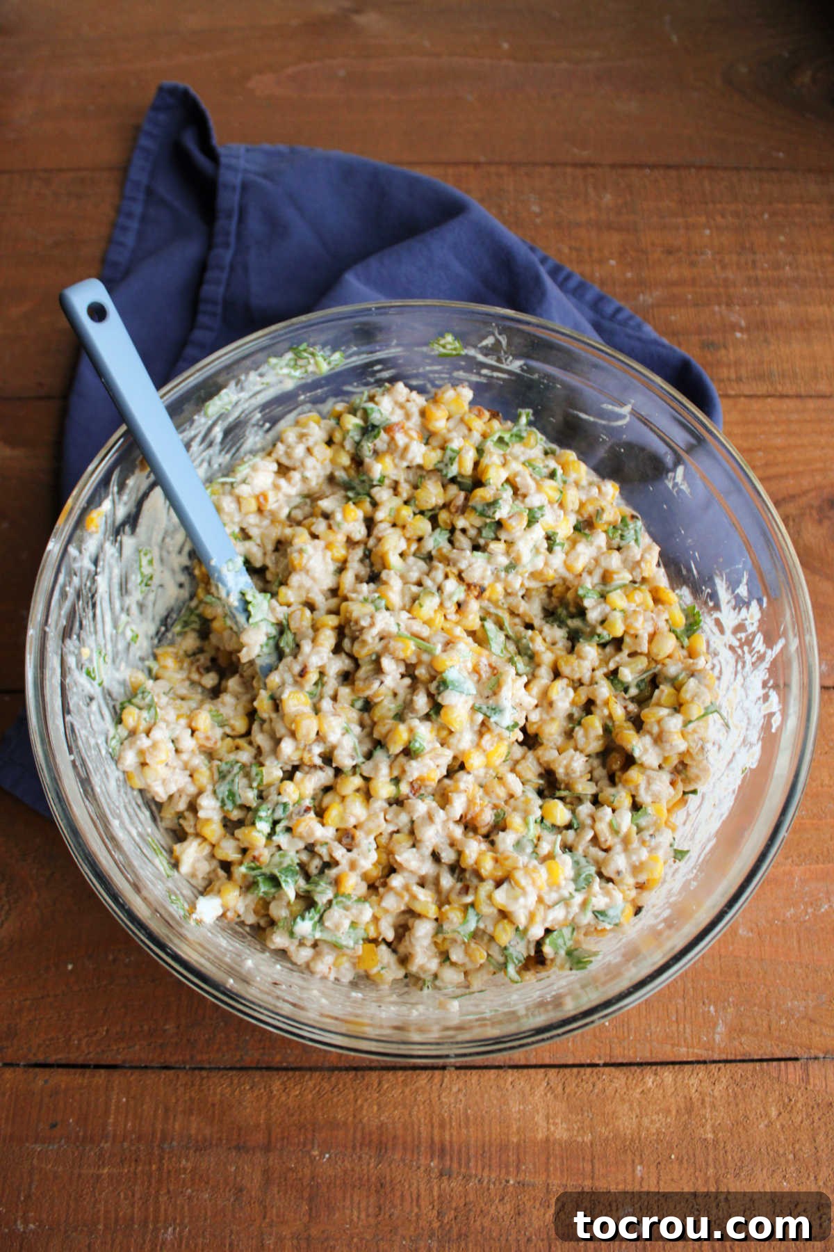 Mixing the Street Corn Barley Salad A large mixing bowl containing cooked barley and charred corn, partially mixed with a creamy, lime-infused dressing, along with fresh green onions and cilantro.