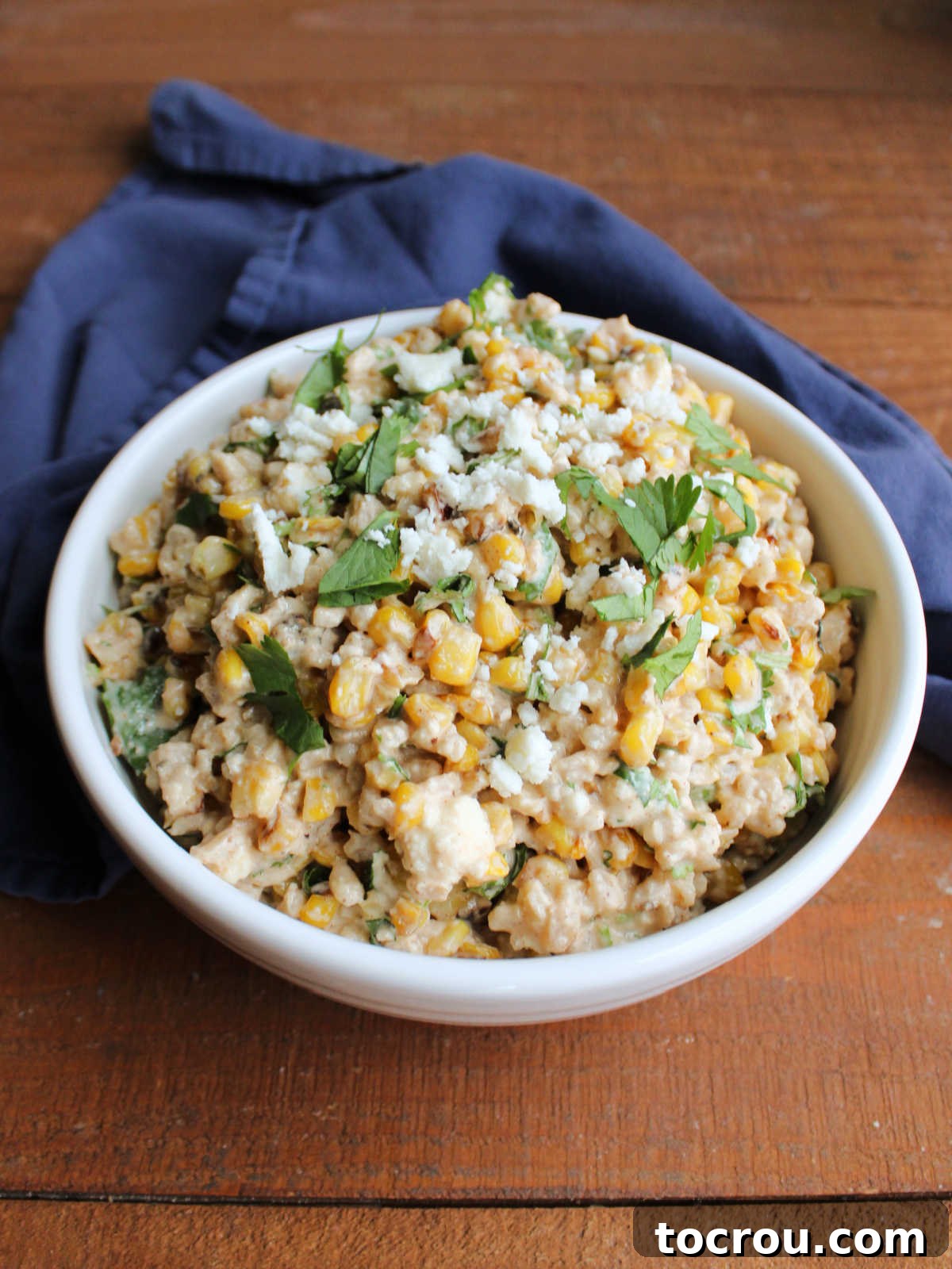 Ready-to-Serve Mexican Street Corn Barley Salad A serving bowl filled with a delightful Mexican Street Corn Barley Salad, adorned with crumbled queso fresco, fresh cilantro, and a lime wedge, ready to be served.