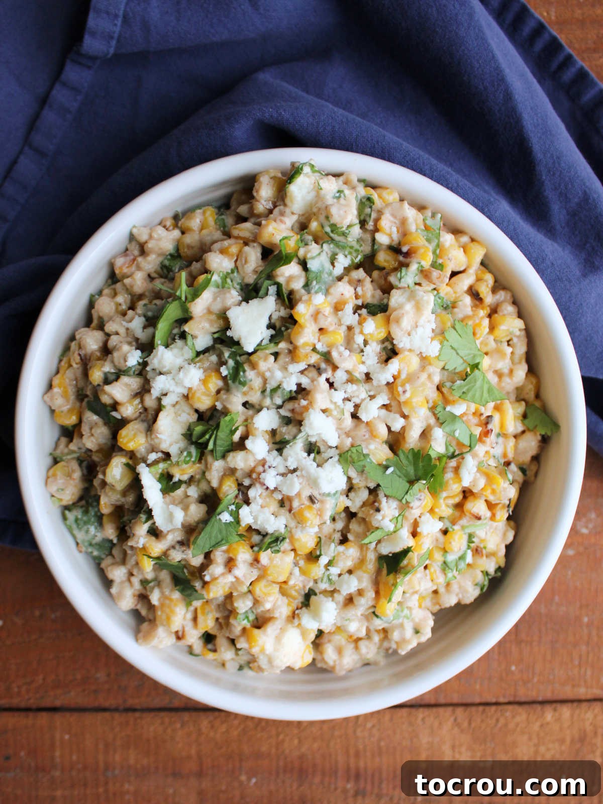 Garnished Mexican Street Corn Barley Salad Close-up view of a serving bowl overflowing with Mexican Street Corn Barley Salad, showcasing the textures of barley, charred corn, and the vibrant garnishes of queso fresco and cilantro.