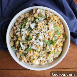 Serving bowl filled with barley and corn salad with creamy dressing, queso fresco, cilantro, and lime, ready to eat.