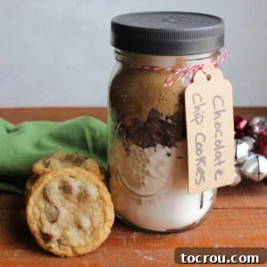 Jar of homemade chocolate chip cookie mix next to a stack of freshly baked chocolate chip cookies.