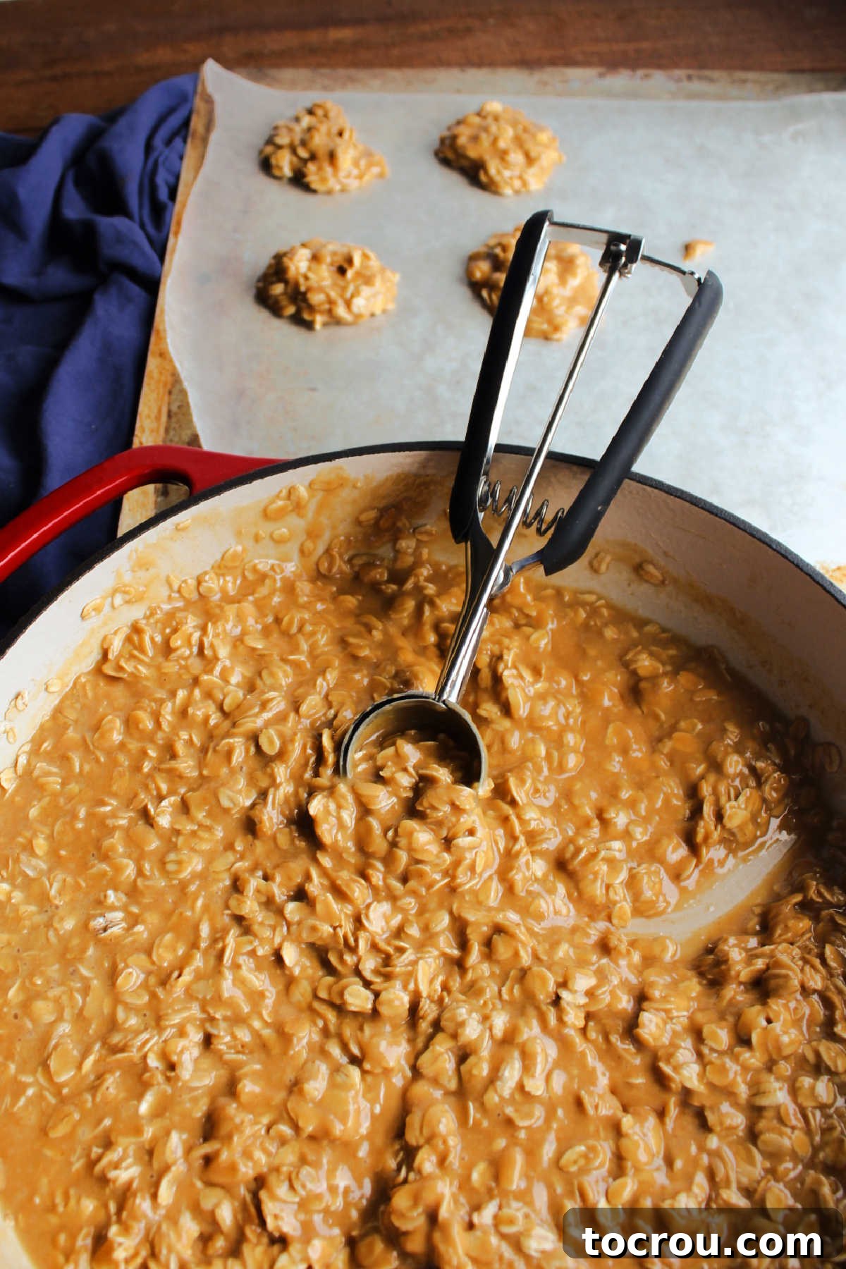 Using a cookie scoop to neatly portion the warm, gooey peanut butter and oatmeal mixture onto a sheet of wax paper, forming individual cookies.