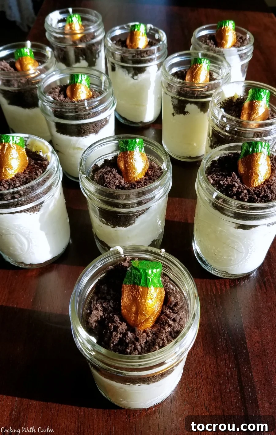 Easter Dirt Pudding Jars with Candy Carrots Jars filled with vanilla pudding mixture and oreo crumbs topped with carrot shaped chocolate candies that look like they are growing in the dirt pudding.