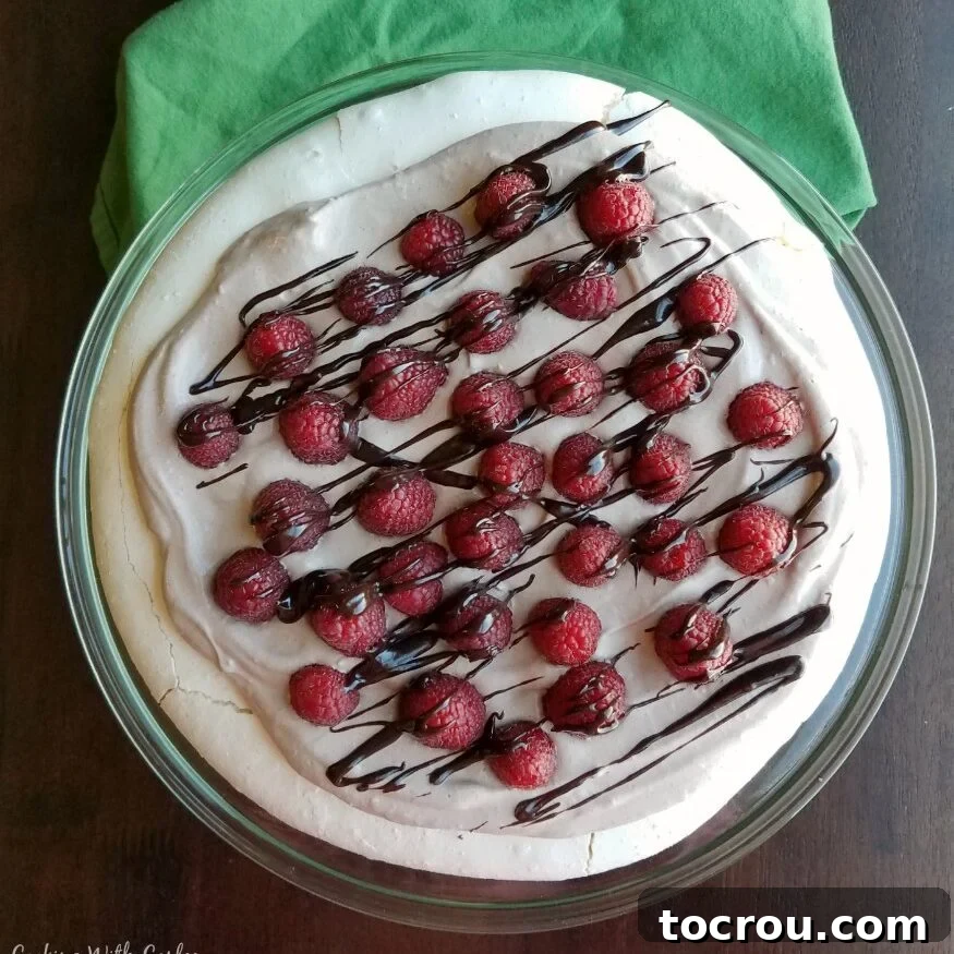 Fluffy meringue pavlova topped with chocolate whipped cream, fresh raspberries and a drizzle of chocolate.