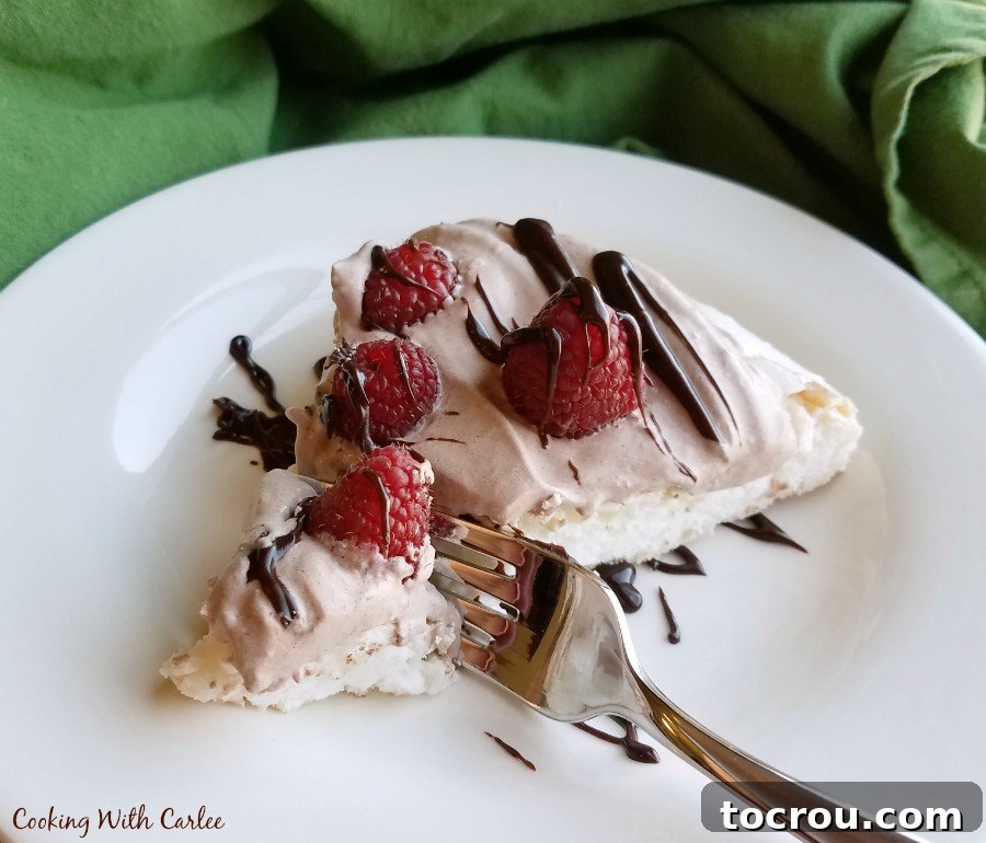 Fork getting a bite of pavlova with chocolate whipped cream and raspberries on top. 