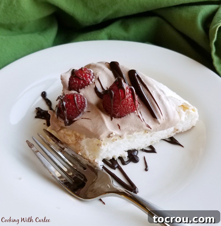 Fork next to a slice of pavlova with fluffy white meringue, chocolate whipped cream, raspberries, and a drizzle of chocolate. 