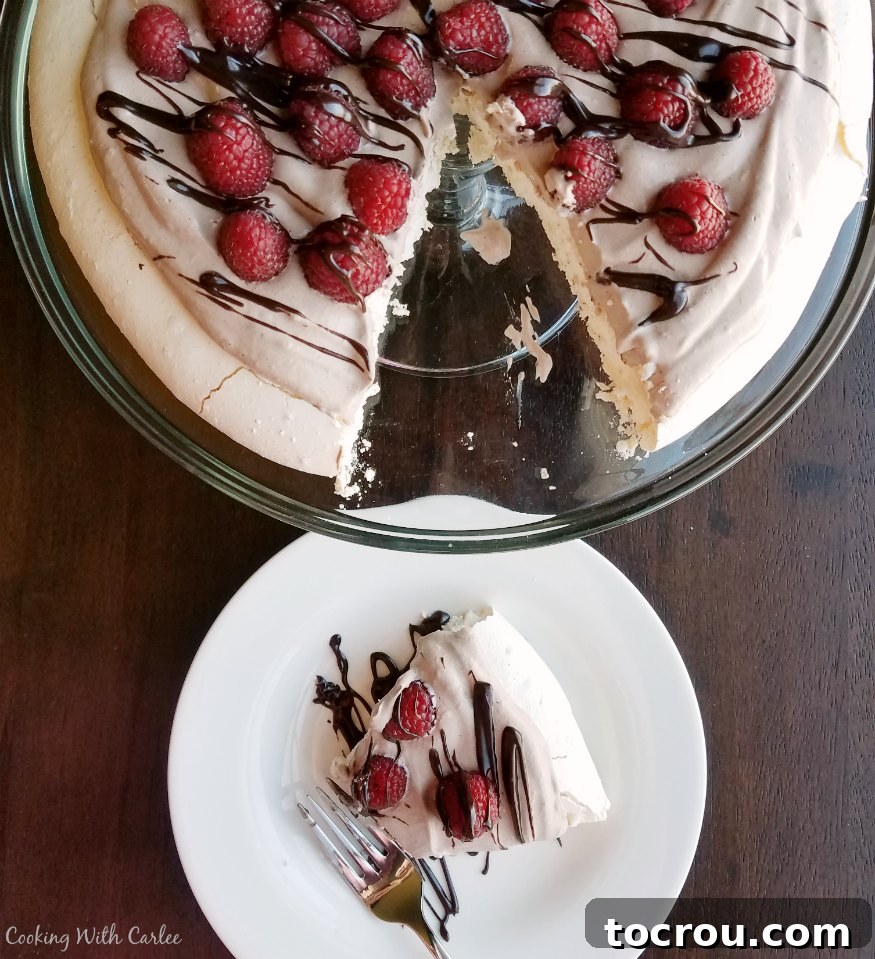 Large pavlova on glass cake stand with a slice on a dessert plate nearby. 