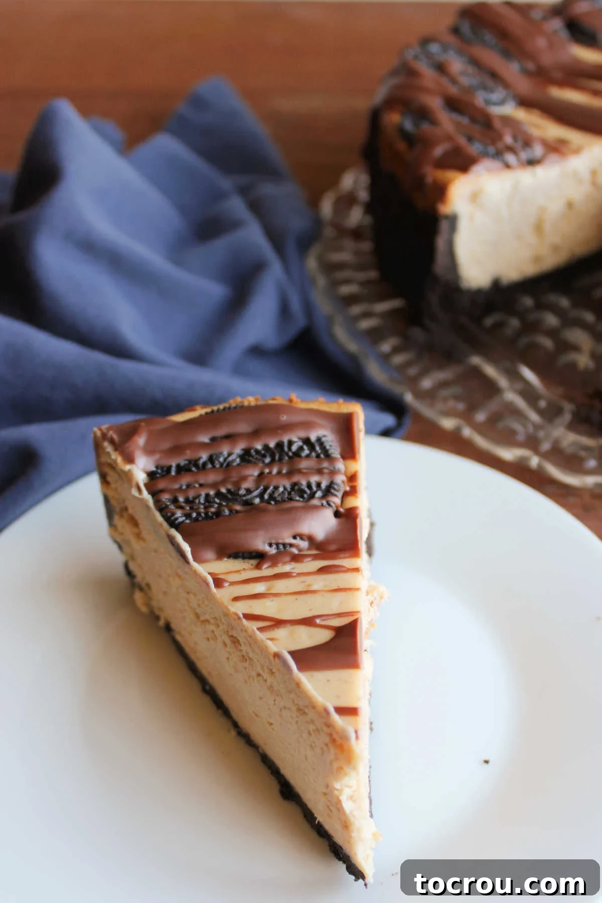 Peanut Butter Oreo Bliss Cheesecake 6 An overhead shot of a slice of peanut butter cheesecake, featuring a whole Oreo cookie baked into the top and a delicate drizzle of chocolate sauce, showcasing its inviting presentation and rich layers.