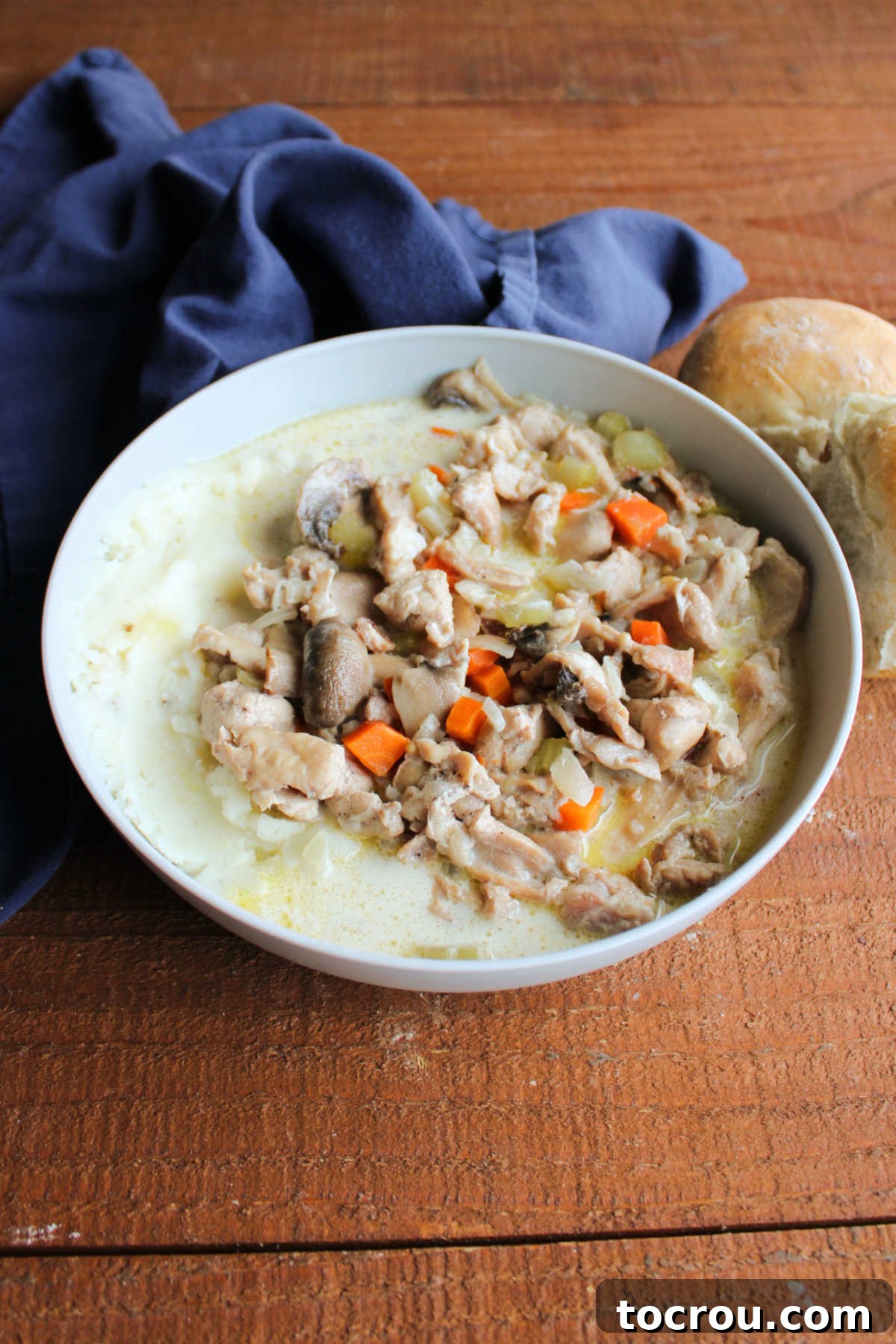A close-up view of a bowl of creamy rabbit stew, showcasing tender chunks of rabbit meat, slices of onion, vibrant carrot pieces, and earthy mushrooms, all nestled in a rich, appetizing broth and served over mashed potatoes, ready to be savored.