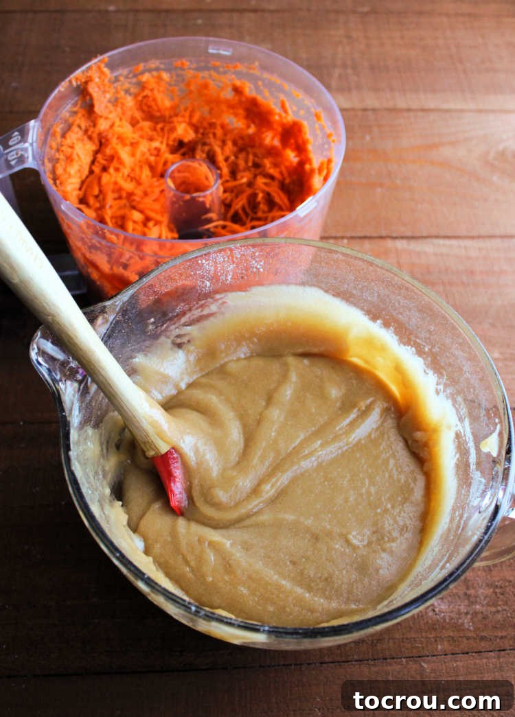 Irresistible Homemade Carrot Cake 5 Bowl of cake batter next to a food processor of grated carrots.