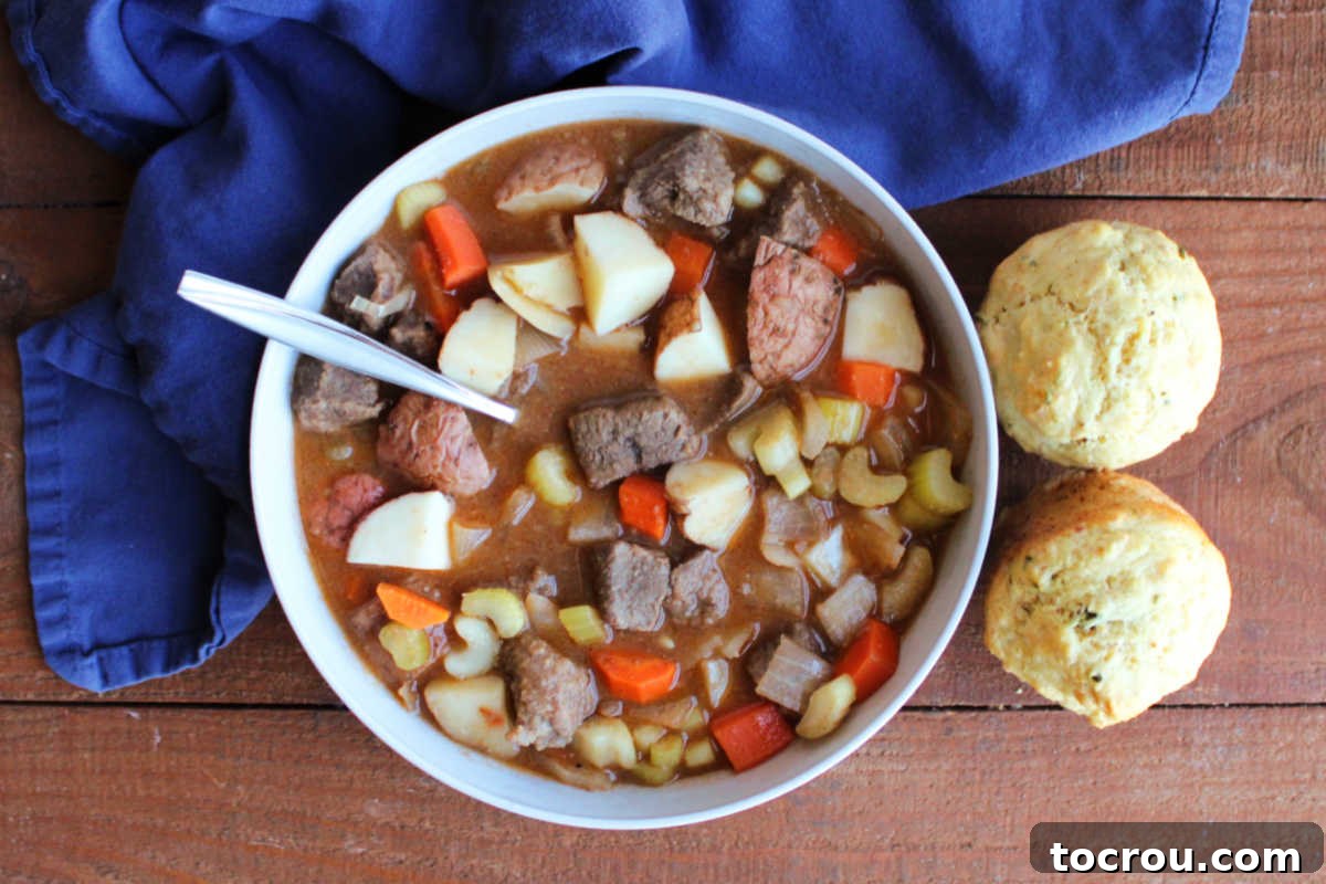 Ready-to-Eat Venison Stew A close-up shot of a bowl of venison stew, showcasing succulent chunks of tender meat and perfectly cooked vegetables in a thick, rich broth. A couple of homemade savory muffins sit nearby, perfect for soaking up every last drop of the delicious liquid.