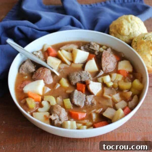Bowl of venison stew with chunks of meat, potatoes, carrots, onions and celery in rich broth with some savory parmesan herb muffins nearby.