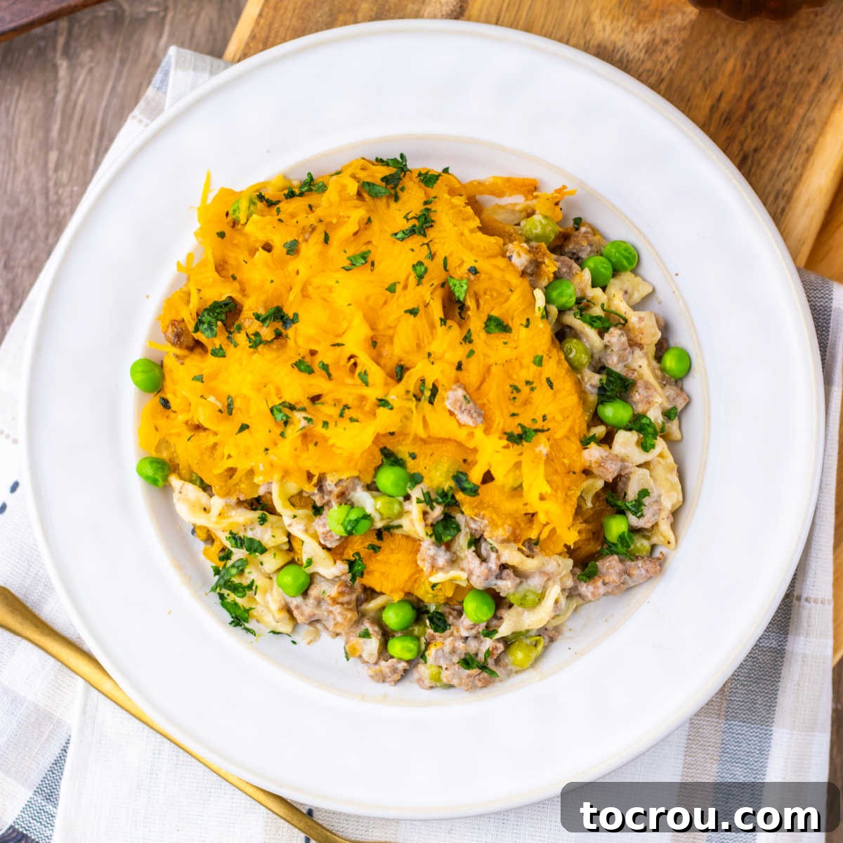 A serving of classic Amish Country Casserole featuring ground beef, wide egg noodles, and green peas in a savory cream of mushroom sauce, topped with bubbling melted cheddar cheese on a white plate, ready to be enjoyed.